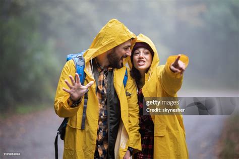 Happy Couple In Raincoats Talking While Walking In Misty Forest High