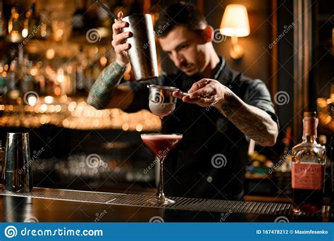 Tattooed Bartender Pouring A Alcoholic Drink From The Steel Shaker To