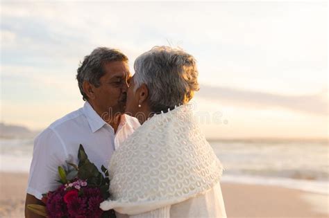 Newlywed Senior Multiracial Couple Kissing Each Other During Wedding Ceremony At Beach Stock