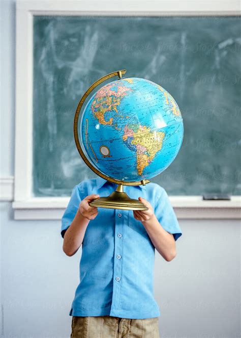 Child Standing In Classroom Holds A Globe Up In Front Of His Face By