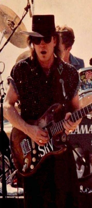 A Man With A Hat And Glasses Playing An Electric Guitar In Front Of