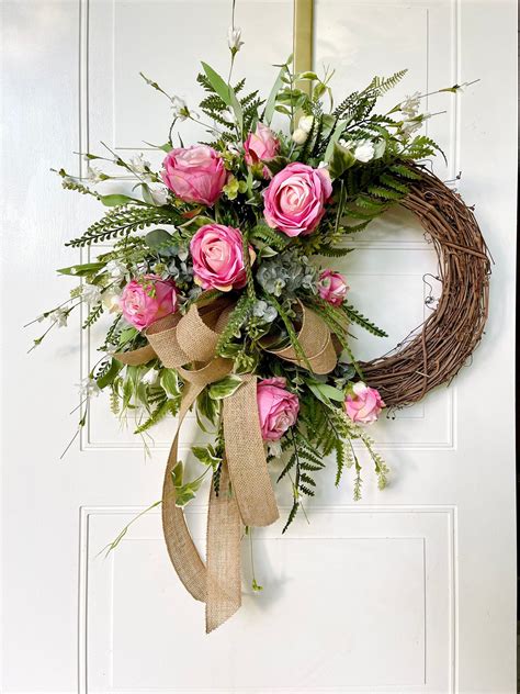 A Wreath With Pink Roses And Greenery Hangs On The Front Door