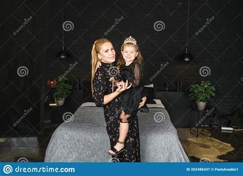 Stylish Mother And Daughter In Black Dresses Indoor A Beautiful Blonde Mother Holding In The