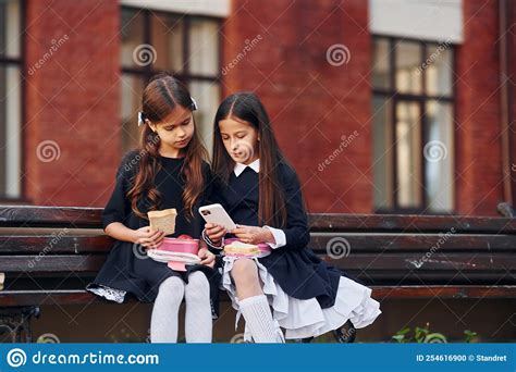 Two Schoolgirls Is Sitting Outside Together Near School Building Stock