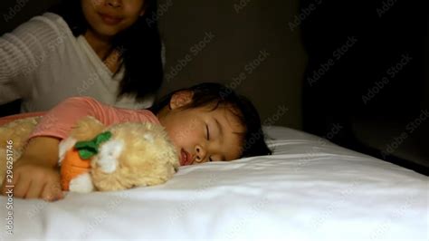 asian mother is putting blanket on her daughter who is sleeping in the bed and goodnight kiss