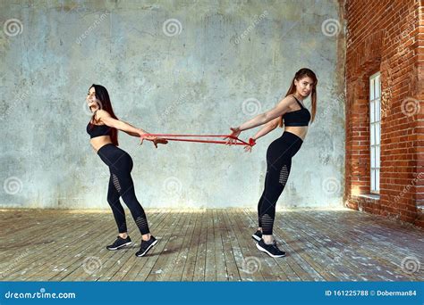 Two Young Women Are Doing Paired Exercises In The Fitness Room Posing And Smiling At The Camera