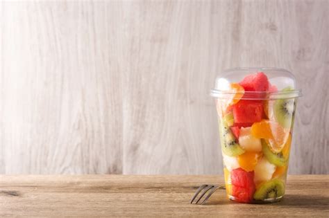 Premium Photo Fresh Cut Fruit In A Plastic Cup On Wooden Table