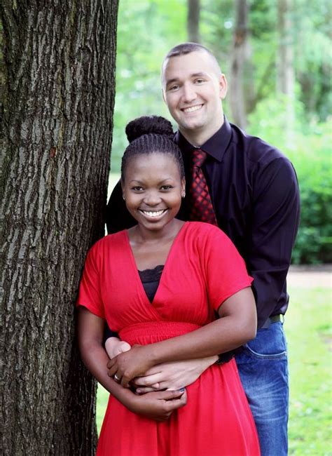 A Man And Woman Standing Next To Each Other In Front Of A Tree With Their Arms Around Each Other