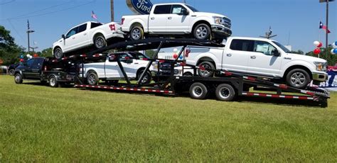Two White Trucks Are On The Back Of A Flatbed Trailer In A Grassy Field