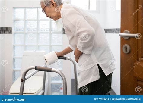 Senior Woman With Diarrhea Holding Tissue Roll Near A Toilet Bowl