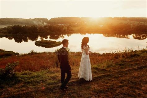 Romantic Landscape Newlywed Couple Posing At Sunset Field Near A Lake