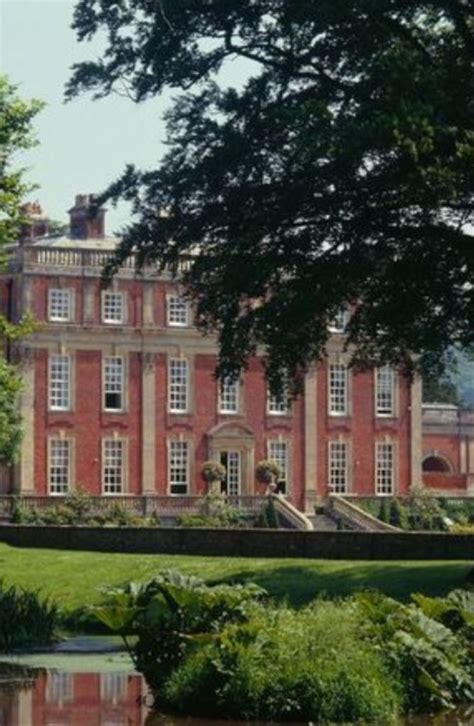 A Large Red Brick Building Sitting On Top Of A Lush Green Field Next To