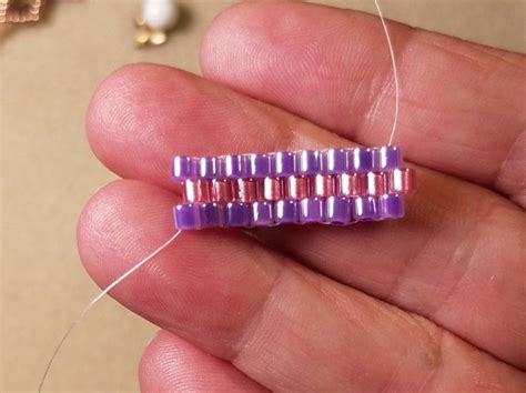 A Hand Holding A Purple Bead On A Thread Spool With Beads In The Background