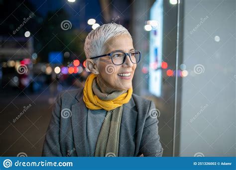 Smiling Mature Senior Woman With Short Gray Hair And Eyeglasses Walking On Street Night Scene