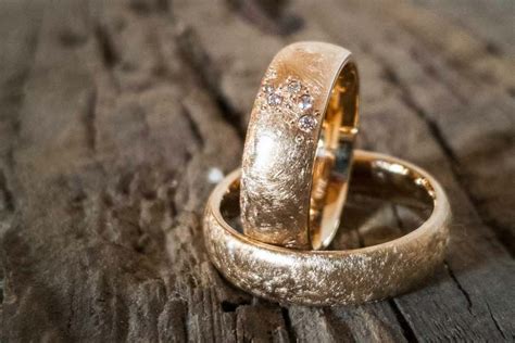 Two Gold Wedding Rings Sitting On Top Of A Wooden Table Next To Another