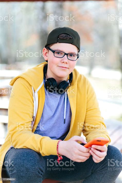 Smiling Handsome Teenage Boy Sitting Holding His Orange Phone Looking