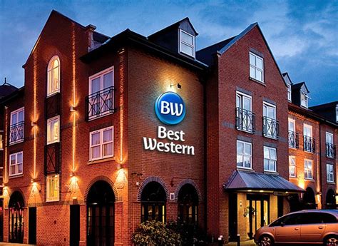 The Best Western Hotel Is Lit Up At Night With Cars Parked On The