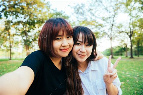 Two Beautiful Happy Young Asian Women Friends Having Fun Together At Park And Taking A Selfie