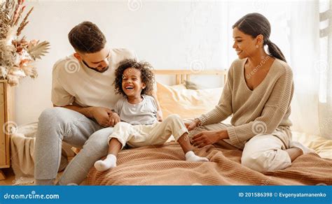 lycklig multietnisk mamma pappa och barn som skrattar och klipper i sängen hemma arkivfoto