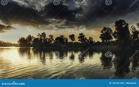 Lake Surrounded By Trees Under A Cloudy Sky And Sunlight During The