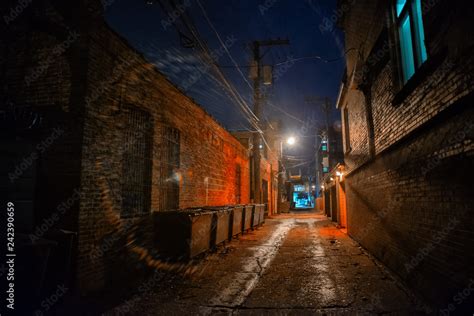 Dark And Eerie Industrial Urban City Alley With Dumpsters At Night In