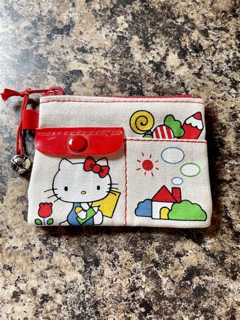 A Hello Kitty Purse With A Red Handle On A Granite Counter Top Next To A Cell Phone