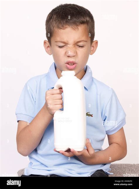 Boy Pulling Face As He Smells Milk In Large Plastic Carton That Has