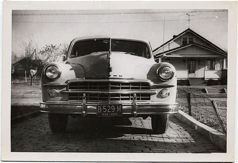 an old black and white photo of a car parked in front of a house on the