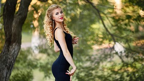 Girl Model Is Wearing Black Dress Standing In Blur Green Trees