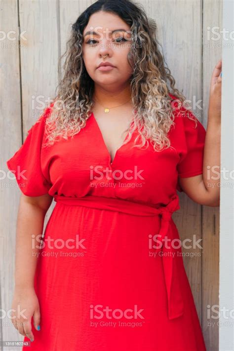 Beautiful Plus Size Model In Red Dress Standing Outdoors Near A Wooden