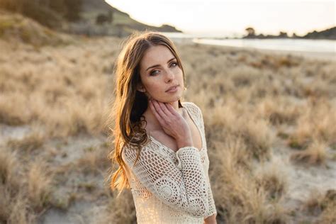 A Woman Is Standing On The Beach With Her Hand Under Her Chin And