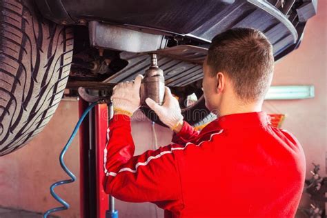 Professional Male Auto Mechanic In Uniform Working Underneath A Stock