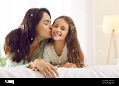 Happy Mother Kisses Her Pretty Little Daughter While Cuddling Together On A Bed At Home Stock