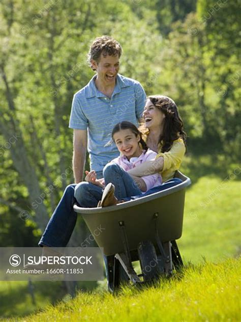 Man Pushing His Daughter And His Wife In A Wheelbarrow Superstock
