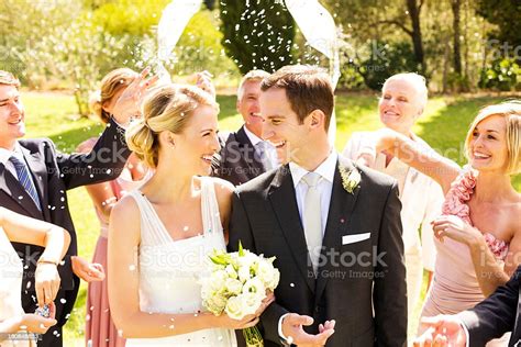 Newlywed Bride And Groom With Guests Throwing Confetti On Them Stock