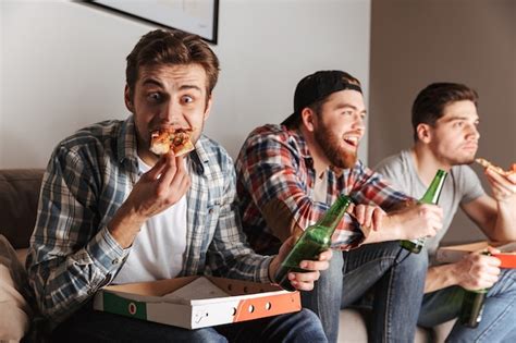 Premium Photo Portrait Of Three Young Bachelors Eating Pizza With Pleasure While Watching
