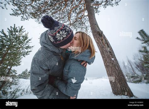 Happy Young Beautiful Couple Kissing Under The Pine Tree In Snowy