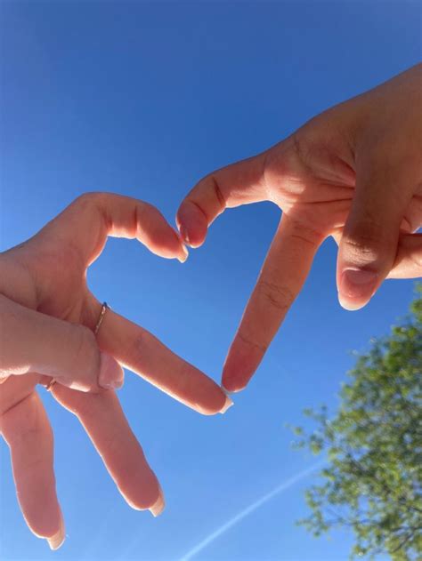 Two Hands Making The Shape Of A Heart Against A Blue Sky With Trees In