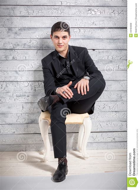 Man In Suit Sitting On Chair With Legs Crossed At Studio Stock Photo