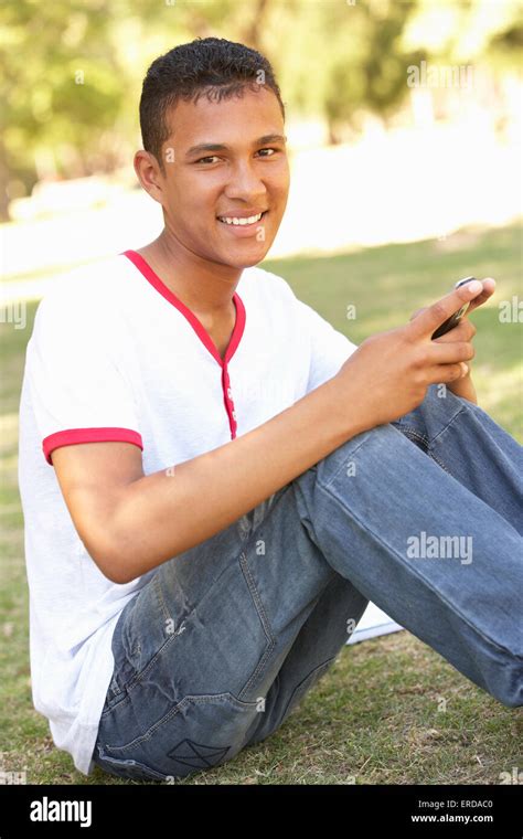 Teenage Boy Sitting In Park Reading Text Message On Mobile Phone Stock