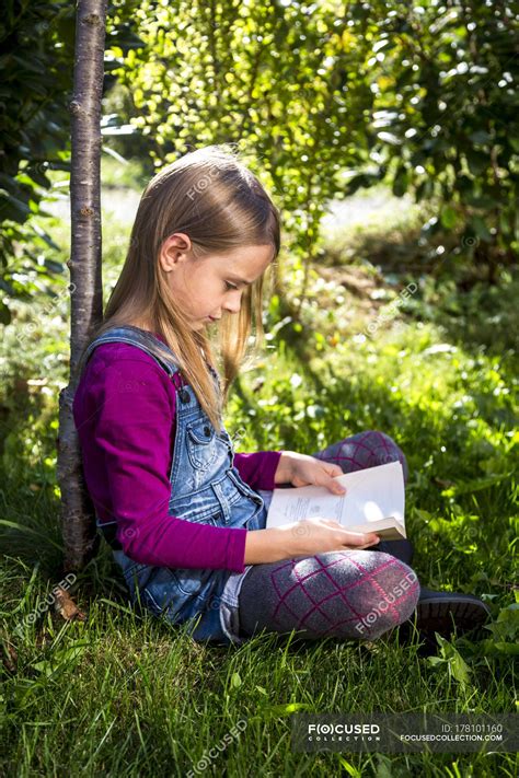 Little Girl Sitting In Garden And Reading Book — Child Side View