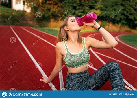 Young Sports Girl Sitting On The Stadium Track And Drinking Water From