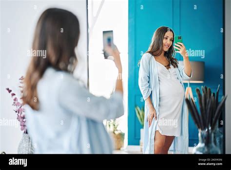 Portrait Of Smiling Pregnant Woman Taking Mirror Selfie At Modern Home