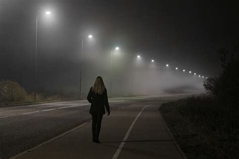 Young Woman Alone Slowly Walking Under White Street Lights In Night