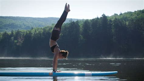 A Person Doing A Handstand On A Surfboard In The Water With Trees In