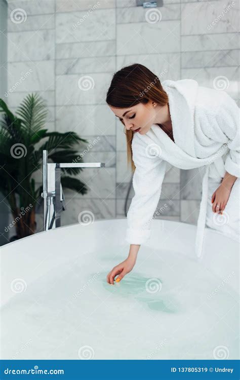 Pretty Slim Woman Wearing Bathrobe Sitting On Edge Of Bathtub Filling