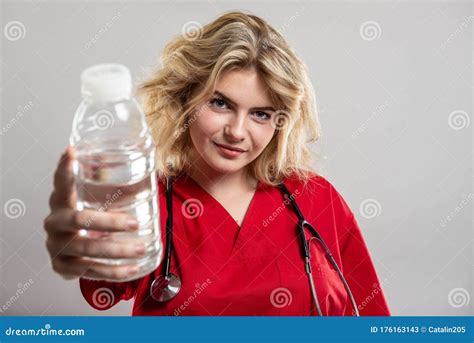 Portrait Of Nurse Wearing Red Scrub Handing Bottle Of Water Stock Image