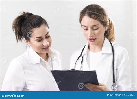 Two Female Assistants Dressed In White Coats Talking To Each Other In
