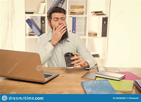 Sleepy Businessman Yawning And Drinking Takeaway Coffee At Office Desk