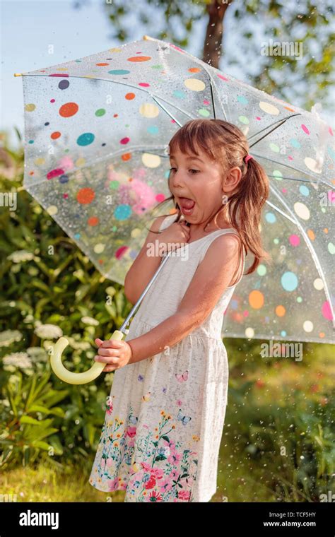 Happy Little Girl Plays In Garden Under The Summer Rain With An